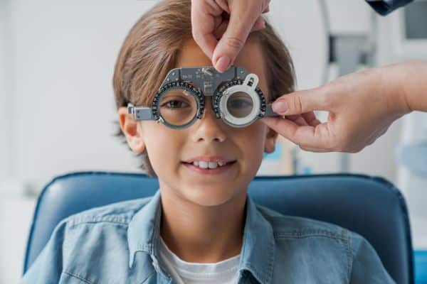 Menino em idade escolar realizando teste de visão em clínica oftalmológica.