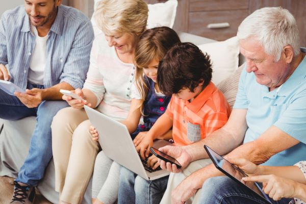Família composta por avós, crianças e jovens sentados no sofá concentrados, cada um, em um aparelho tecnológico. Conceito de distração passiva.