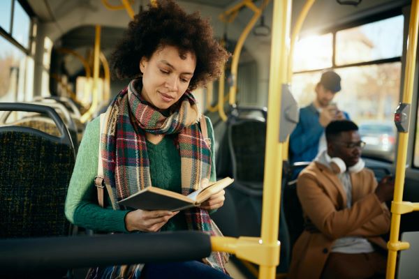 Jovem negra lê enquanto trafega em um ônibus.