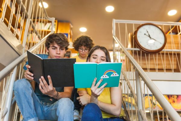 Adolescentes sentandos na escadaria de uma grande livraria , lendo livros.