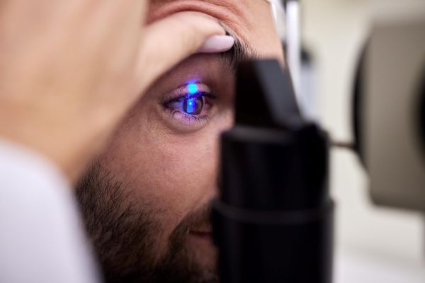 Homem realizando exame de mapeamento de retina frente a um aparelho tecnológico.