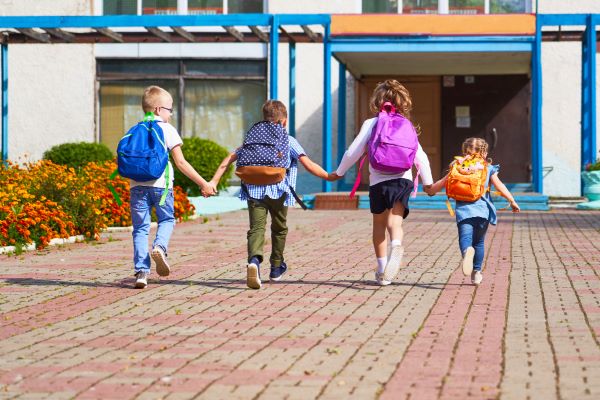 A volta às aulas é motivo de felicidade para quatro crianças do ensino fundamental que correm para a escola com suas mochilas escolares nas costas.
