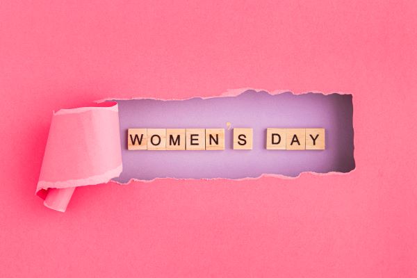 Papel rosa, rasgado no centro, em cujo fundo se encontra a expressão WOMEN'S DAY.