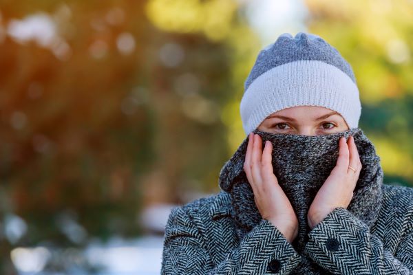 Mulher jovem protege-se do frio do inverno usando casaco de lã e manta cinzas, e também uma toca de lã branca e cinza-claro sobre os cabelos.