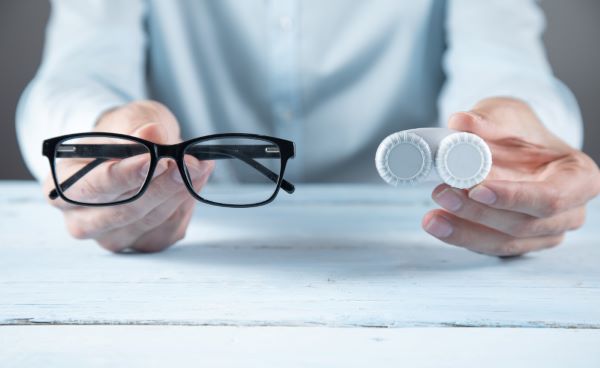 Nas mãos de um homem estão duas opções de correção da miopia: um par de óculos e um par de lentes de contato.