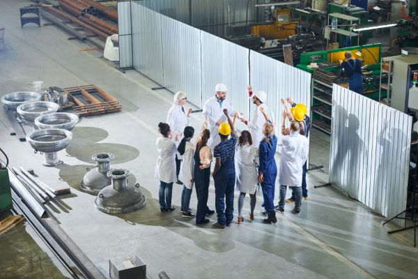 Grupo de profissionais em um ambiente de fábrica reunidos em círculo, demonstrando segurança no trabalho realizado.