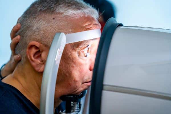 Homem idoso apoiando a cabeça no scanner para verificar o glaucoma.