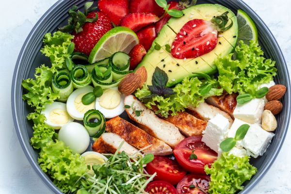 Alimentação saudável com carnes de frango grelhadas, abacate, queijo, ovos de codorna, morangos, nozes e alface.