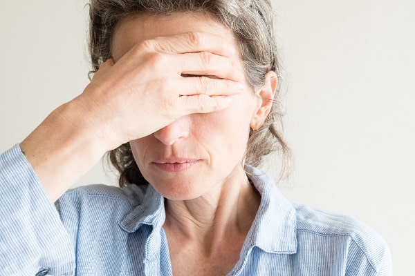 Mulher de meia idade demostrando desconforto ocular ao esfregar a mão sobre os olhos.
