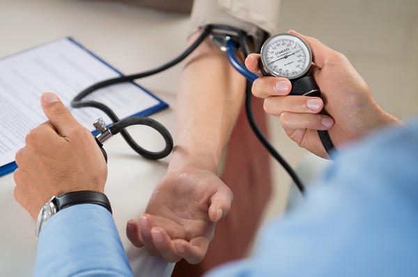 Close das mãos de um médico que afere a pressão de paciente que se encontra com o braço estendido na maca. 
Uma das formas de prevenir-se da neuropatia óptica é controlar a hipertensão. 