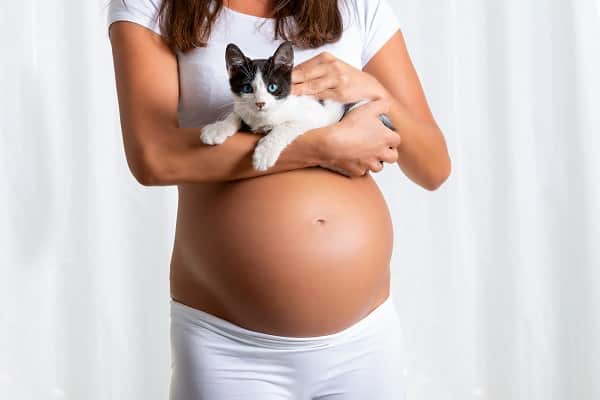 Imagem de mulher grávida segurando um gatinho no colo.