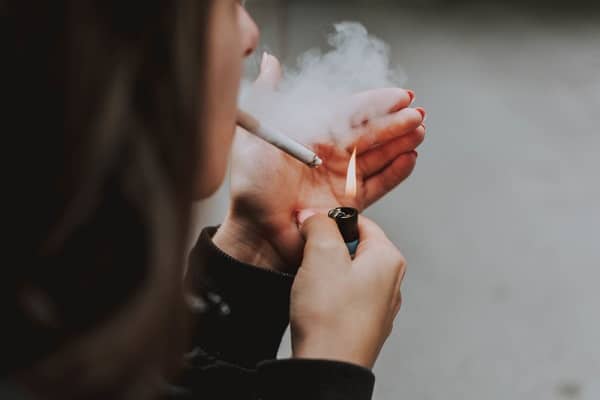 Mulher acendendo um cigarro. Uma das causas da degeneração macular é o tabagismo.