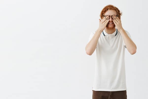 Rapaz ruivo esfrega os olhos com as mãos após ter enxergado pontinhos brancos na parede branca as famosas moscas volantes.