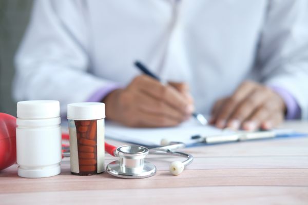 Medicamentos dispostos sobre a escrivaninha na qual um médico faz uma prescrição.