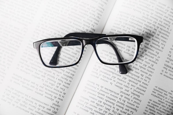 Um par de óculos de grau com aro preto deitado sobre um livro aberto.