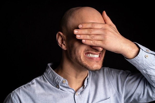 Homem com expressão de dor nos olhos; ele os cobre com uma das mãos.