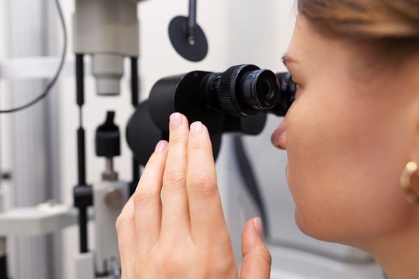 Médica testando a visão de paciente com o uso de instrumento oftalmológico.