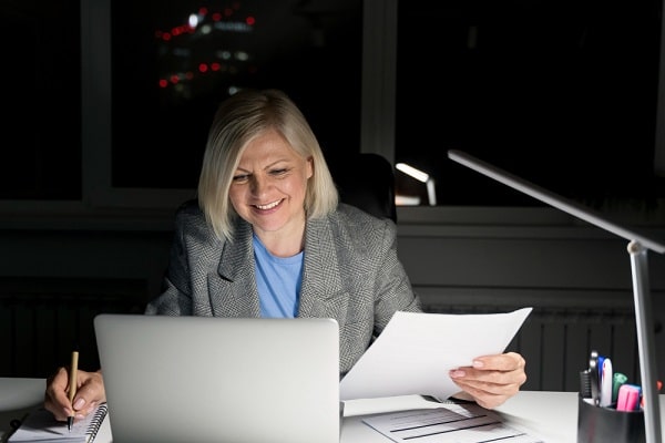 Empresária lendo relatórios em seu escritório com baixa iluminação.