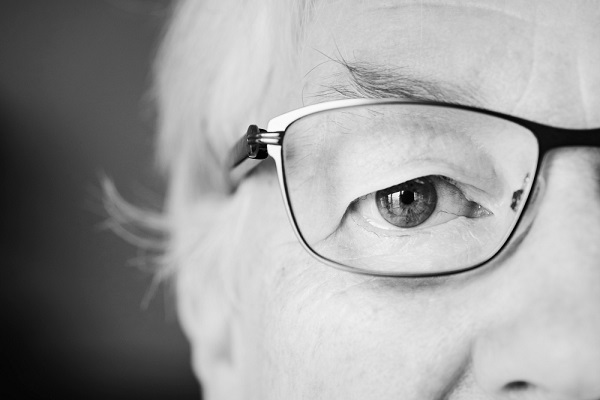 Close up em preto e branco do olho direito de uma mulher idosa que usa óculos de grau.